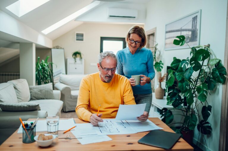 Senior couple sitting at table and looking into blueprints of their new home